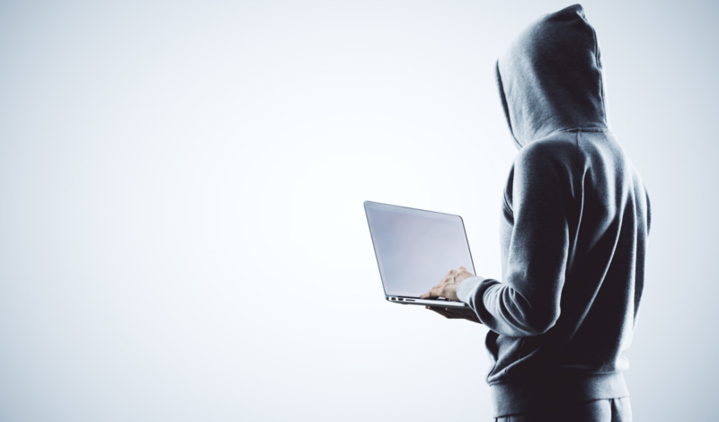 Obscured man in hoodie on laptop