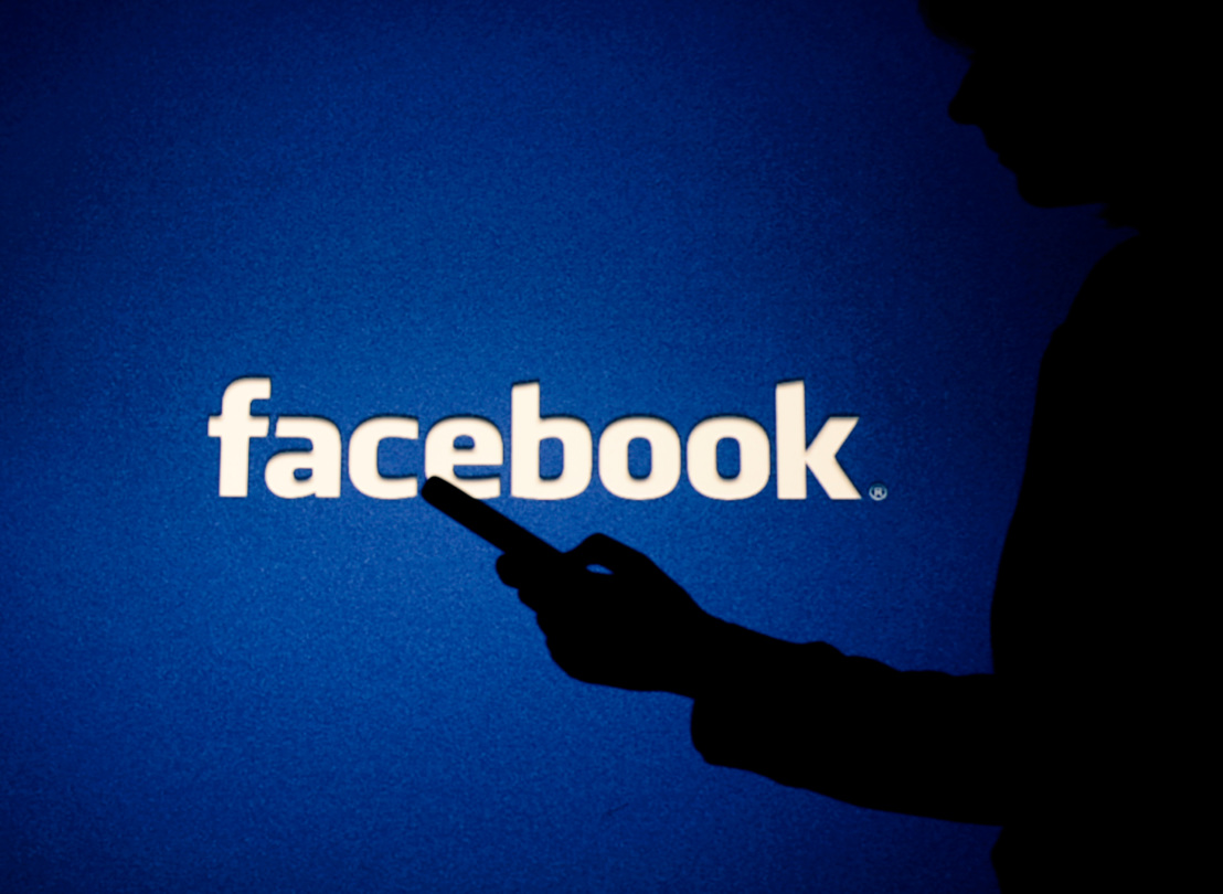 Facebook logo with person holding phone in silhouette