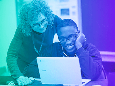 The photo shows a smiling teacher looking over a student's shoulder at their laptop together. The photo has a green-to-purple gradient overlay.