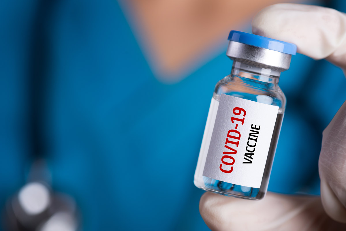 Stock image of a doctor in scrubs holding up a vial labelled 