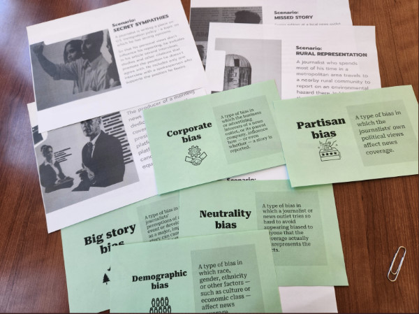 Green and white notecards describing corporate bias, partisan bias, neutrality bias, demographic bias and big story bias, along with scenarios involving news media bias, are spread out on a table.