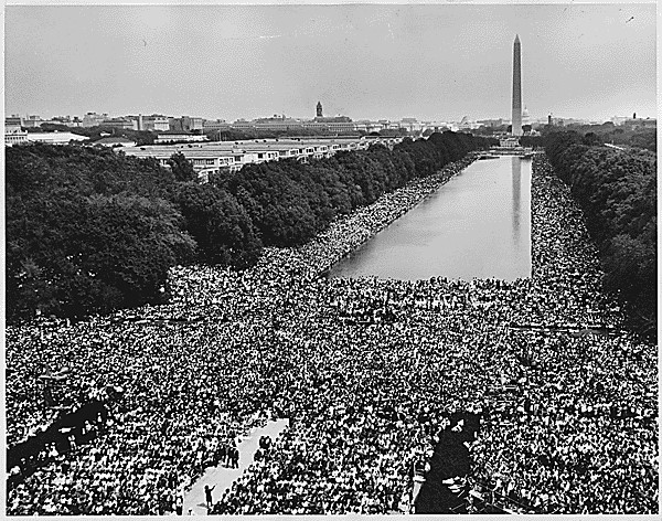 A black-and-white aerial photo of crowds surrounding the Washington Monument and its reflecting pool during the March on Washington in 1963.