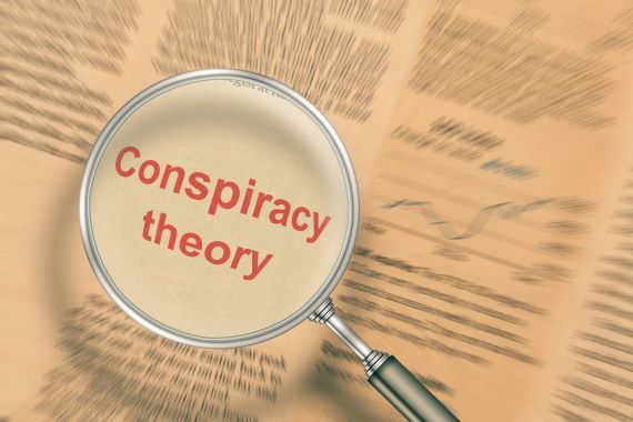 An illustration of a magnifying glass over blurred text reveals the words “conspiracy theory.”