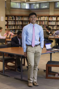 High school student stands up smiling at the camera, in school library