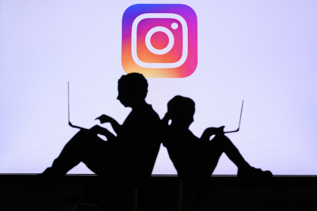 A silhouette of two children sitting back-to-back with laptops. In the background is an enlarged Instagram app icon.