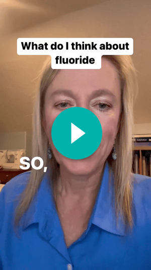 A screenshot of a video of a woman in a blue shirt facing the camera. Text says, “What do I think about fluoride” and “So,”. A teal play button is over the woman’s face.