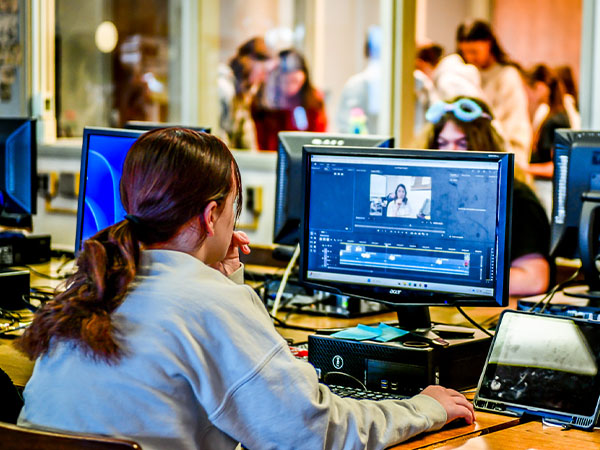 A media literacy and journalism student at Weir High School analyzes video content on her screen as several other students work on their projects in the background.